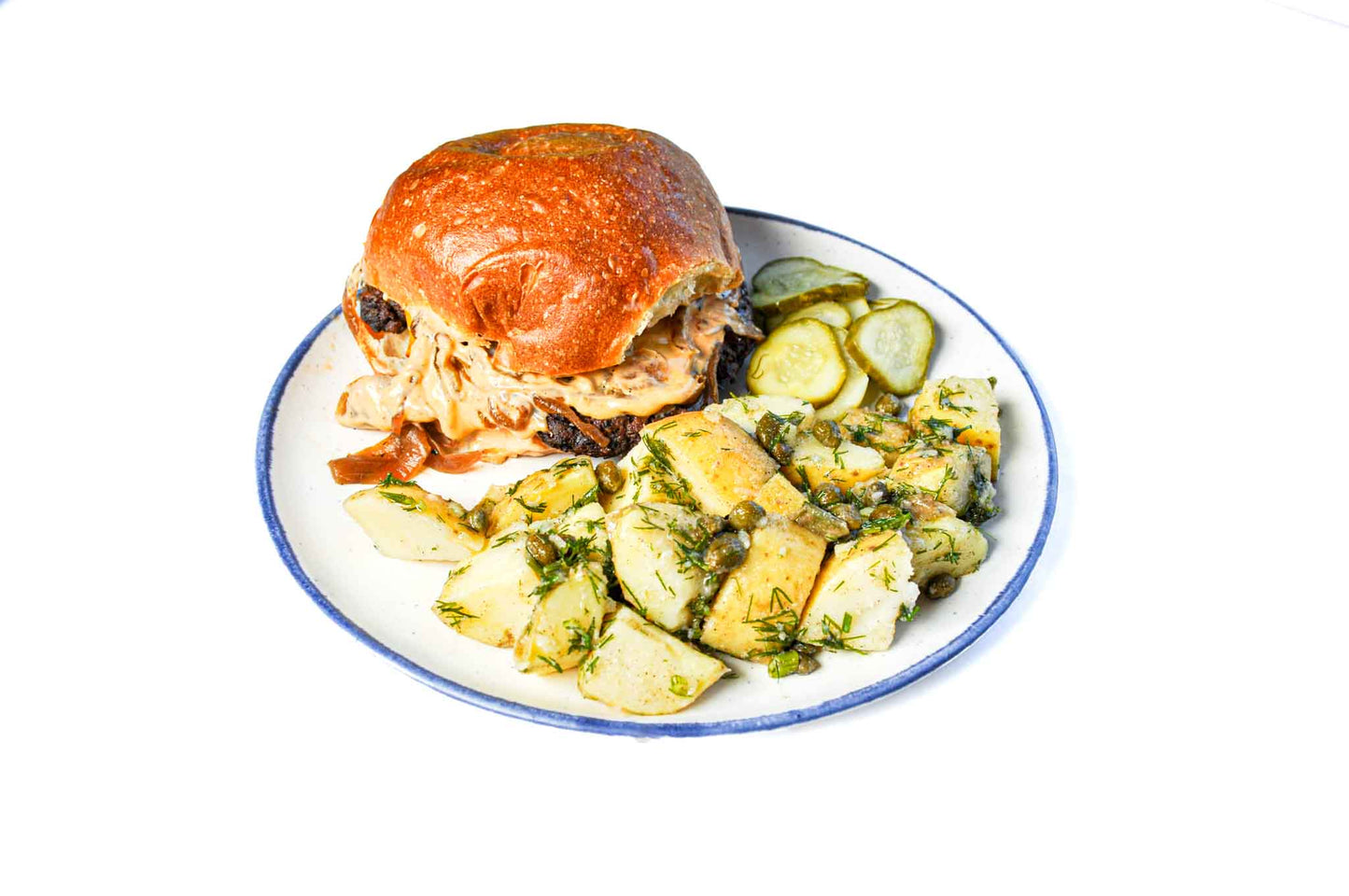 NomNom Burger's Smash Burger on a Brioche Bun features a juicy, perfectly seared patty topped with sweet caramelized onions, served on a soft brioche bun. Accompanied by a creamy potato salad, this dish offers a delightful combination of savory and sweet flavors with a satisfying, hearty texture.