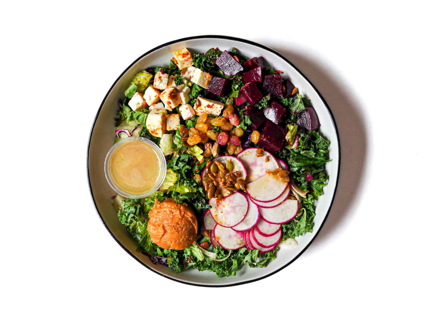 Saucy Greens' Beet and Feta Salad is a delightful blend of spicy potato spread, marinated feta, beets, radish, sunflower, and pumpkin seeds. Crowned with pickled apricot, it sits on a bed of crisp kale and romaine, topped by a tantalizing saucy vinaigrette.