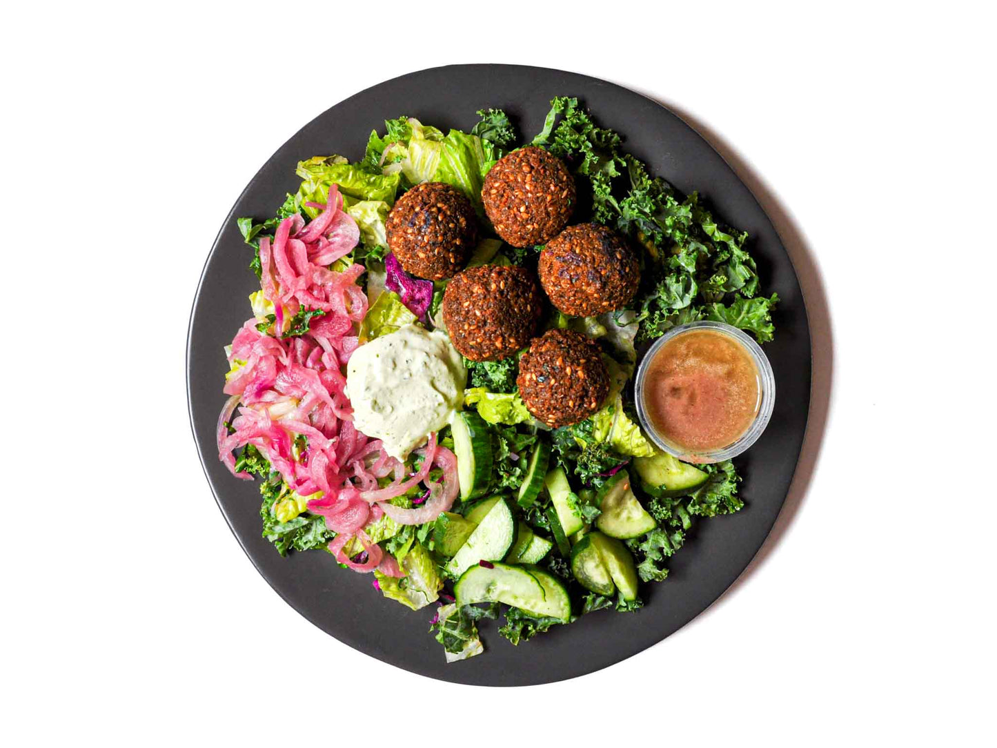 Saucy Green's Falafel Salad features falafel balls crafted from chickpeas, parsley, and aromatic spices. Fresh herb labneh, marinated cucumbers, red cabbage, and onions infuse each bite with tangy zest.