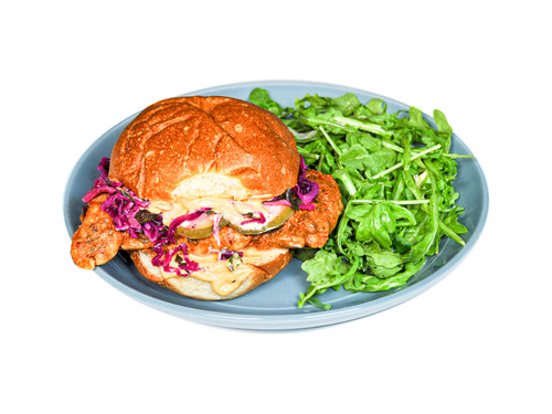 Sumac's Roasted Chicken Sandwich features tender, flavorful roasted chicken layered with crisp red cabbage slaw, paired with a refreshing arugula fennel salad. This dish offers a satisfying blend of savory, crunchy, and peppery flavors, making for a delicious and well-rounded meal.