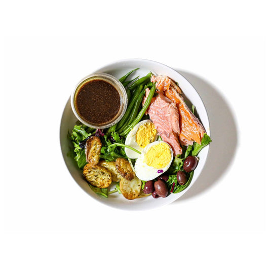 Buddha Bowl's Salmon Niçoise Salad features tender salmon atop a bed of fresh greens, accompanied by crisp green beans, briny Kalamata olives, and a medley of other classic ingredients. This dish offers a delightful combination of savory, fresh, and tangy flavors, creating a refreshing and satisfying meal that's perfect for any time of day.