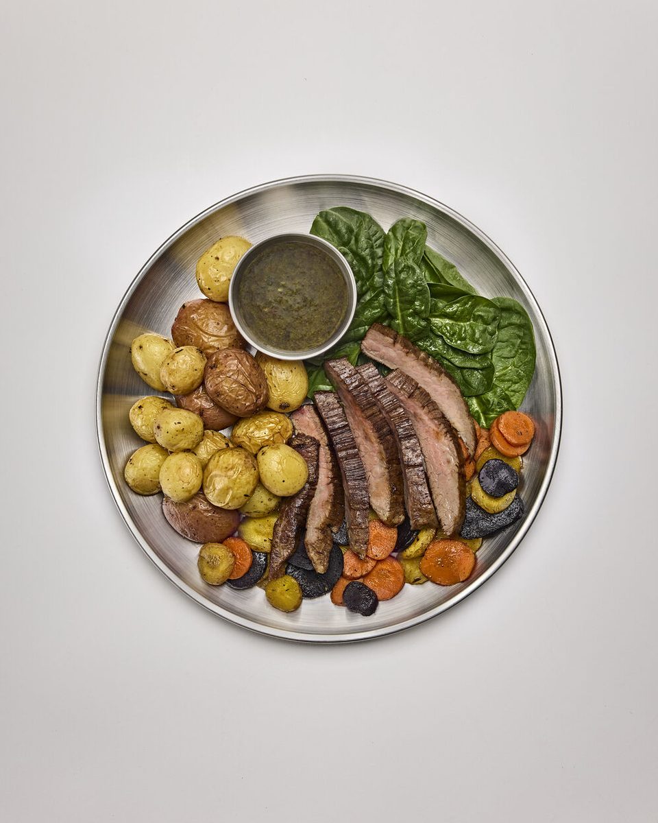 Grass-fed steak with potatoes and greens on a steel plate